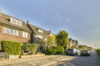 Yan tarafında arabalar ve arkada evler olan bir cadde, yol boyunca bazı ağaçlar büyüyor.