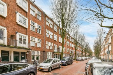 Amsterdam, Hollanda - 10 Nisan 2021: üzerinde balkotlar olan bazı apartmanların önünde cadde kenarına park edilmiş arabalar