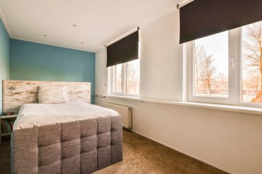 Penceresinde mavi duvarlar ve beyaz süslemeler olan bir yatak odası, farklı tonlarda boyanmış.