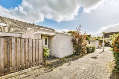 Fotoğrafta ahşap çitli ve beyaz tuğlalı bir ev olan arka bahçe alanı yerden sokağa çekiliyor.