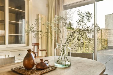 Arka bahçesinde cam bir kapı ve avlu olan ahşap bir masadaki vazoda çiçekler.