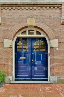 Kırmızı tuğlalı bir binanın önündeki mavi bir kapı üzerinde kemerli bir pencere ve kapılar açık.