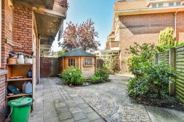 Amsterdam, Hollanda - 10 Nisan 2021: Bahçesinde bazı bitkiler ve diğer şeylerin bulunduğu arka bahçe kırmızı tuğla duvarlarla çevrili, yeşil çöp görülebilir