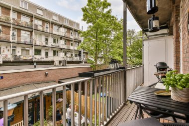 Veranda dışında sandalyeler, masalar ve bitkilerle dolu bir balkon bir apartmandan sokağa bakıyor.