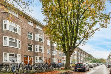 Amsterdam, Hollanda - 10 Nisan 2021: Birçok pencere ve bant olan tuğla bir apartmanın önündeki caddenin kenarına parketmiş bisikletler
