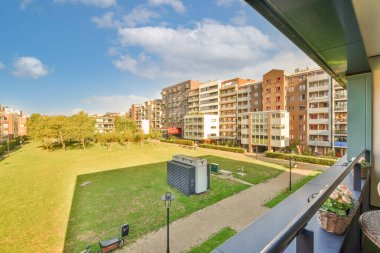 Arka planda binalar ve fotoğrafın diğer tarafında yeşil çimenler olan bir dış alan açık mavi gökyüzü.