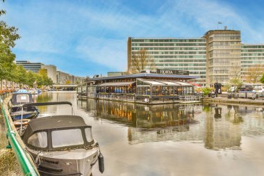 Amsterdam, Hollanda - 10 Nisan 2021: Arka planda binalar ve rıhtıma yanaşmış teknelerin yanında yürüyen insanlar olan bir tekne.