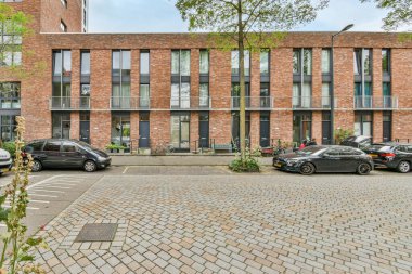 Amsterdam, Hollanda - 10 Nisan 2021: Her iki tarafında birçok penceresi olan tuğla bir binanın önüne park edilmiş iki araba ve kameraya bakan bir araba