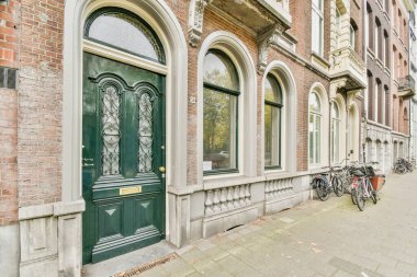 Tuğla bir binanın yanındaki yeşil bir kapının önünde kemerli pencereleri ve kapıları olan iki bisiklet.