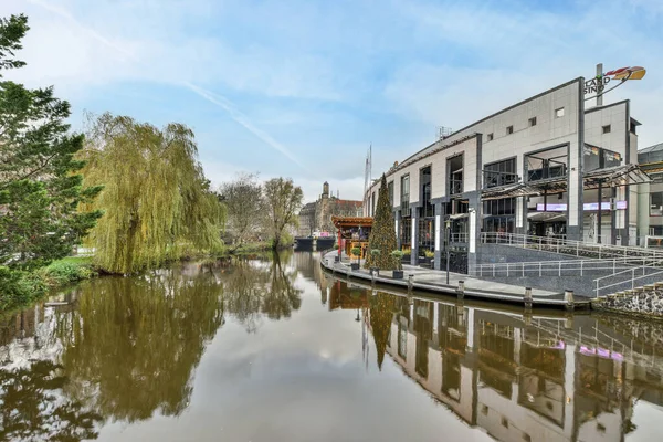 stock image a canal with buildings and trees in the fore, taken from the waters edge on a clear blue sky day