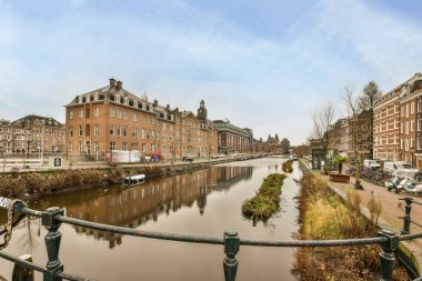 Amsterdam, Hollanda - 10 Nisan 2021: Her iki tarafında binalar ve su bulunan bir kanal, üstten geçen bir köprüden alındı.