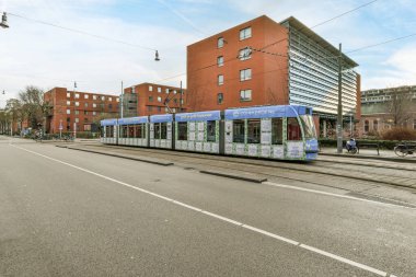 Amsterdam, Hollanda - 10 Nisan 2021: Pencerelerinin üzerinde mavi ve beyaz tente olan turuncu bir binanın önündeki bir otobüs