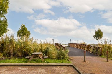 Amsterdam, Hollanda - 10 Nisan 2021: Köprüye giden üst geçitten geçen bir yol üzerinde banklar, ağaçlar ve çimenler olan bir park