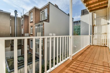 Güneşli bir günde arka planda beyaz korkuluklu ve kırmızı tuğlalı evler olan bir balkon.