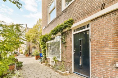 Yan tarafında bitkiler büyüyen tuğla bir bina ve önünde küçük bir verandaya açılan açık bir kapı.