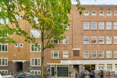 Amsterdam, Hollanda - 10 Nisan 2021: Birçok pencere ve balyası olan bir apartmanın önünde caddenin kenarına park edilmiş bazı arabalar