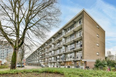Amsterdam, Hollanda - 10 Nisan 2021: Önünde ağaçlar ve çalılar olan bir apartman dairesi, açık mavi bir gökyüzü gününde