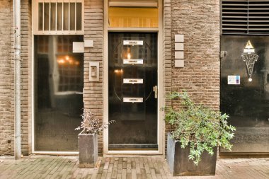 Ön kapının yanında iki saksı ve önünde de kaldırım olan tuğla bir bina.