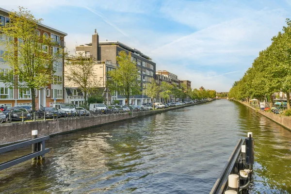 stock image a canal in the middle of an urban area with buildings and trees on both sides there is a blue sky