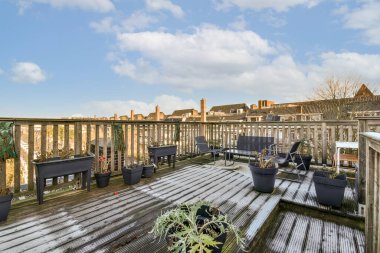 Ahşap güvertede saksı bitkileri ve arka planda binalar olan bir çatı, yukarıdan çekilmiş.