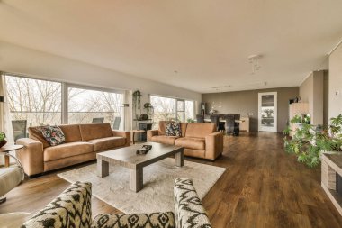 Oturma odası, koltuklar, sandalyeler ve büyük pencerelerin önündeki sehpa sokağa bakıyor.