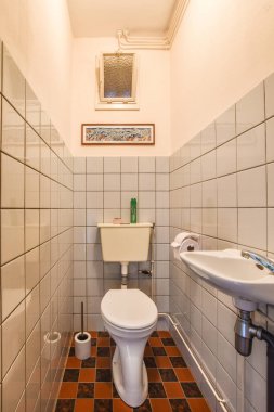 Amsterdam, Hollanda - 10 Nisan 2021: Banyoda fayanslı duvarlar ve yerde kırmızı fayanslar olan bir tuvalet, tuvaletin yanında lavabo var.