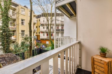 Arka planda ağaçlar ve binalar olan bir dış alan. Balkondan çekilmiş. Bal apartmanlarından birine bakıyor.