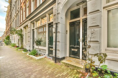 Amsterdam, Hollanda - 10 Nisan 2021: yanında bitkiler ve çiçekler büyüyen bir binanın önündeki tuğla kaldırım