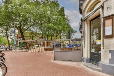 Amsterdam, Hollanda - 10 Nisan 2021: Bir binanın önündeki yolun kenarına park etmiş bir bisiklet insanların yürüdüğü ve etrafında oturduğu