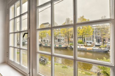 Amsterdam, Hollanda - 10 Nisan 2021: Bazı tekneler açık bir pencereden nehrin karşı kıyısındaki kanala ve binalara bakıyor.