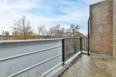 Beyaz boyanmış bir binanın yan tarafında tuğla duvar ve siyah metal parmaklıklar olan bir dış alan.