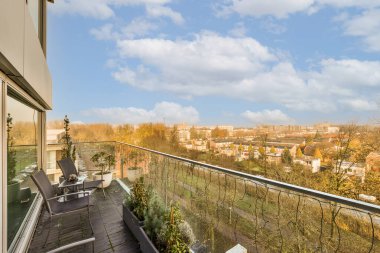 Güneşli bir günde bir apartmanın penceresinden görüldüğü gibi, uzakta ağaçlar ve binalar olan bir balkon.