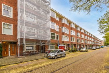 Amsterdam, Hollanda - 10 Nisan 2021: Kenarında arabalar olan bir şehir caddesi ve onları güneşten korumak için plastik ambalajlarla kaplı binalar