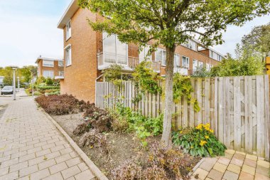 Amsterdam, Hollanda - 10 Nisan 2021: Tuğla duvarları ve ön bahçesinde ağaçlarla çevrili ahşap çitlerle çevrili bir evin dış görünüşü