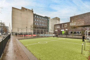 Amsterdam, Hollanda - 10 Nisan 2021: Şehir merkezinin ortasında bir futbol sahası ve arkasında binalar ve insanlar oynuyor.