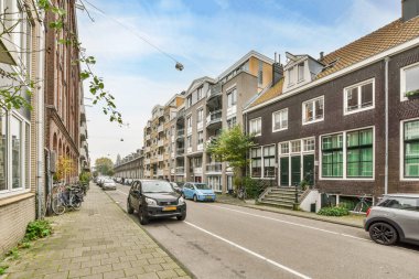 Amsterdam, Hollanda - 10 Nisan 2021: kaldırım boyunca dizilmiş bazı binalar ve bisikletlerin önünde yol kenarına park edilmiş bir şehir caddesi
