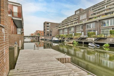 Amsterdam, Hollanda - 10 Nisan 2021: Tekne iskelesine giden köprüsü olan bir apartmanın önündeki su üzerinde bazı binalar ve tekneler