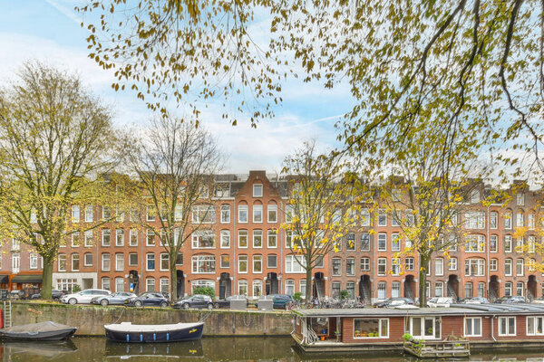 Amsterdam, Netherlands - 10 April, 2021: some boats in the water and buildings on the other side of the river with leaves hanging from trees over them