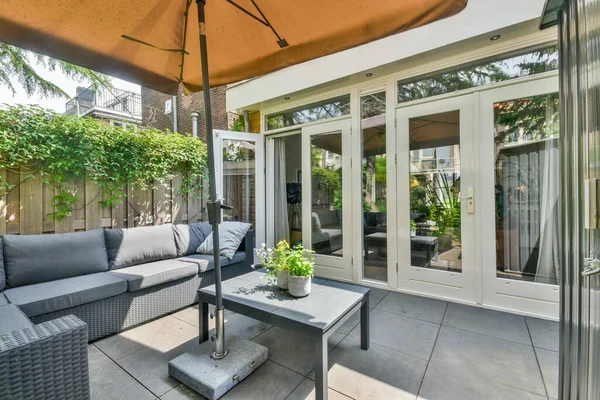 stock image a patio with an umbrella over the couch and coffee table in front of the door to the back yard area