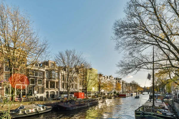 Amsterdam, Hollanda - 10 Nisan 2021: her iki tarafında tekneler ve evler olan bir kanal, teknelerden diğer tarafı gösteriyor.