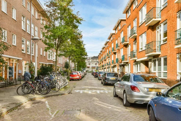 Stock image some cars parked on the side of a bricked street in an urban area with many buildings and bicycles lined up against each other