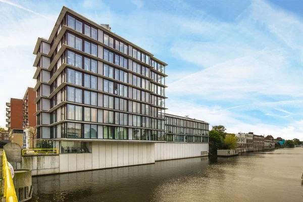 stock image a building on the side of a body of water with buildings in the background and people walking along the river