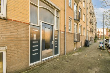 Önünde arabalar park edilmiş tuğla bir bina ve başka bir binaya açılan açık bir kapı.