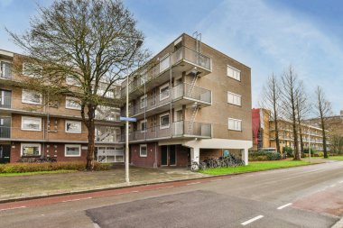 Önünde bisikletleri olan bir apartman dairesi ve kaldırımda ağaçlar var.