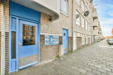 Amsterdam, Hollanda - 10 Nisan 2021: Apartman bloğunun yanına park edilmiş bir arabanın önündeki tuğla binanın mavi kapısı