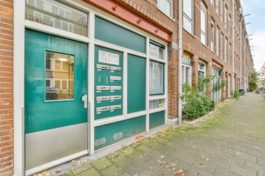 Amsterdam, Hollanda - 10 Nisan 2021: Beyaz boya ile boyanmış ve kentsel bir alanda bulunan tuğla bir binanın yanındaki yeşil kapı