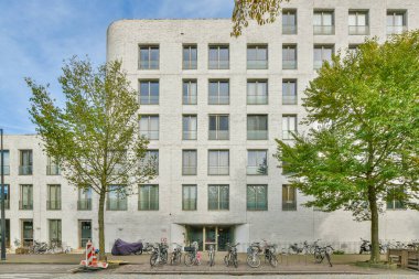 Amsterdam, Hollanda - 10 Nisan 2021: Bazı motosikletler büyük beyaz bir binanın önüne park edilmiş ve etrafında birçok pencere var.