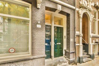 Yeşil kapılı ve camları beyaz çerçeveli tuğla bir bina. Önündeki kaldırım boyunca.