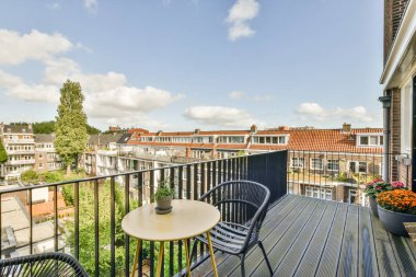 Amsterdam, Hollanda - 10 Nisan 2021: İki sandalyeli bir balkon ve sol tarafında bir masa, arka planda mavi bir gökyüzü var.