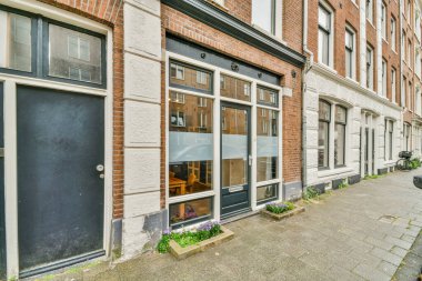 Şehrin ortasında bir tuğla bina. Caddenin kenarında bitkiler ve çiçekler yetişiyor.